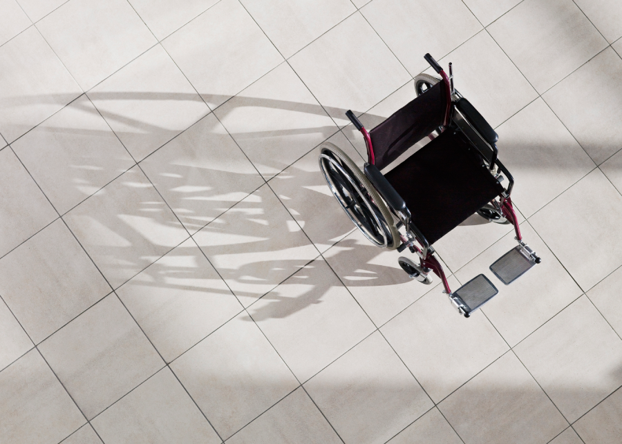 Empty wheelchair casting a shadow on tiled floor.