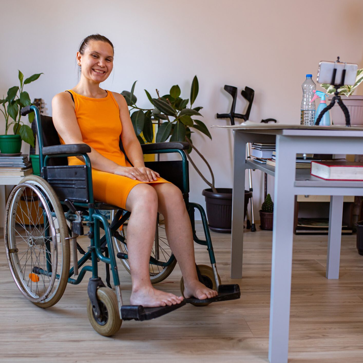 A smiling woman in an orange dress sitting in a wheelchair indoors.